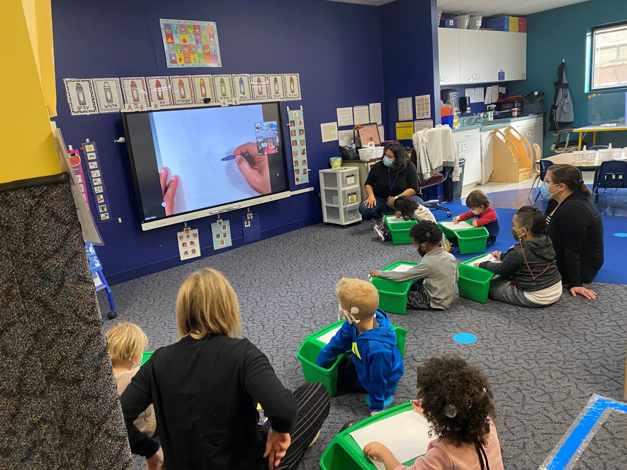 Young children on classroom floor watching an artist draw