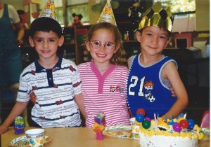 Three children in party hats with a birthday cake