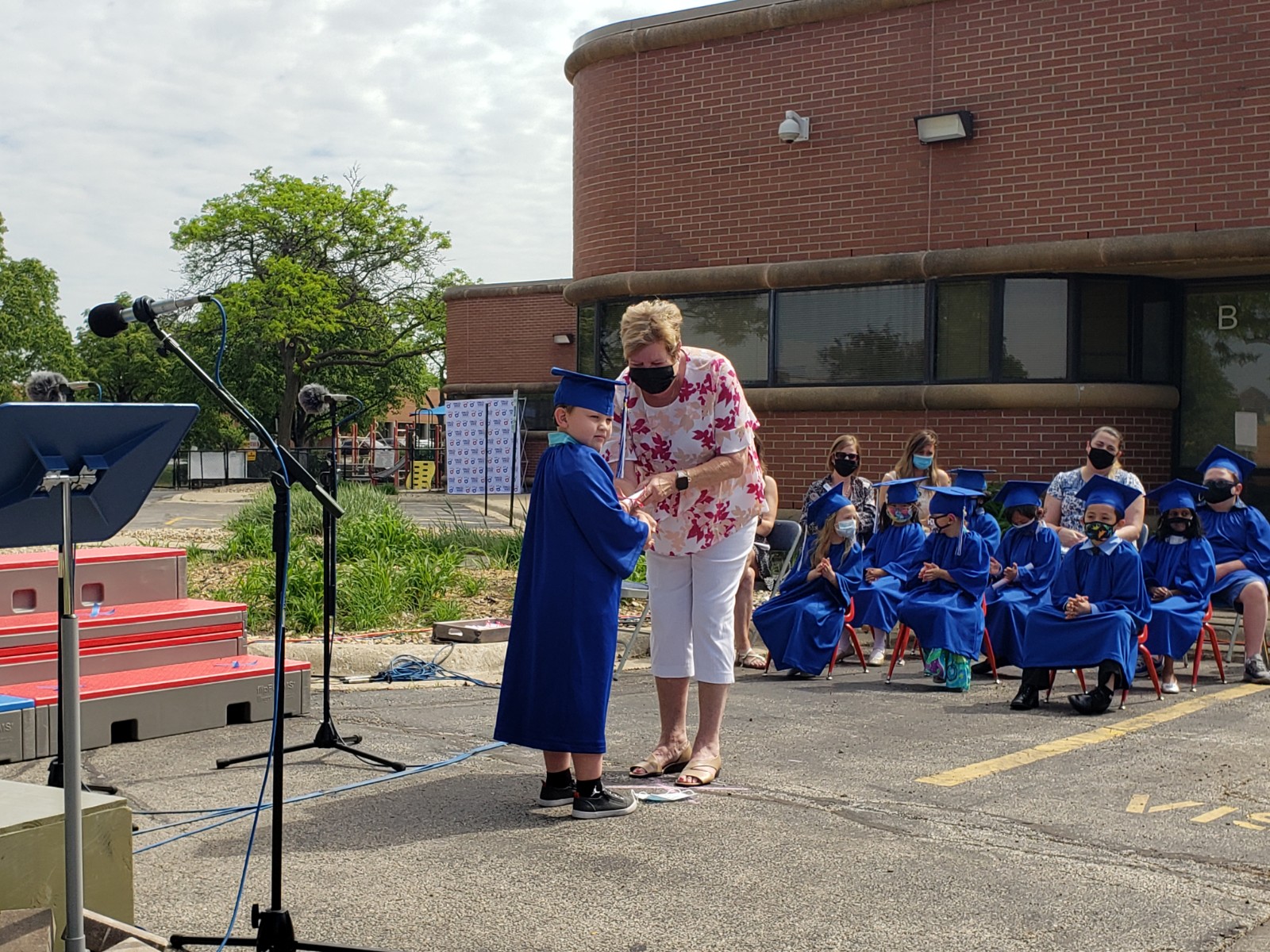 Woman handing child in blue graduation cap and gown a diploma