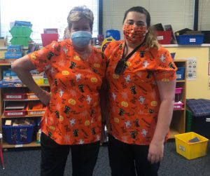 Two women with masks in orange Halloween scrubs