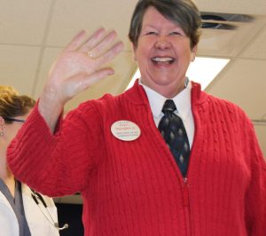 Woman dressed as Mr. Rogers in red sweater, waving
