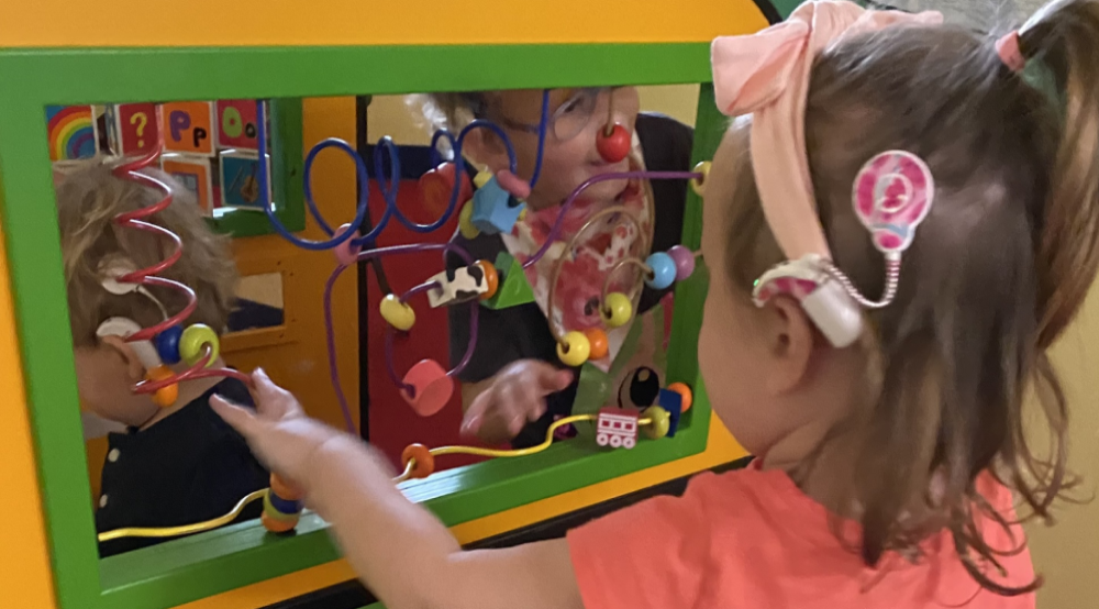 young girl wearing a cochlear implant plays on an activity board