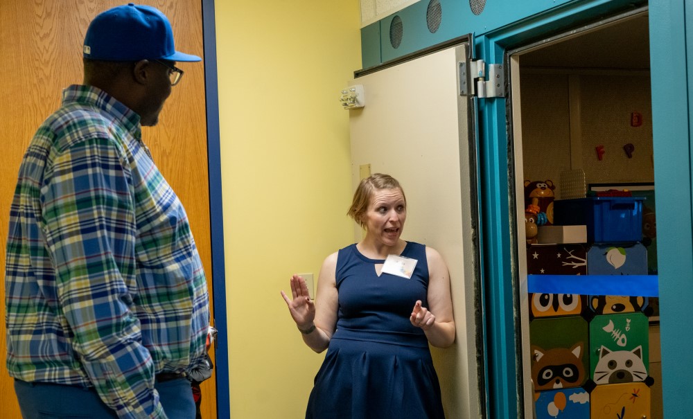 A woman in a blue dress gives a tour of a medical office to a man in a checked shirt