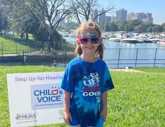 Young girl in a tye-dyed shirt and sun glasses smiles along Lake Michigan in Chicago