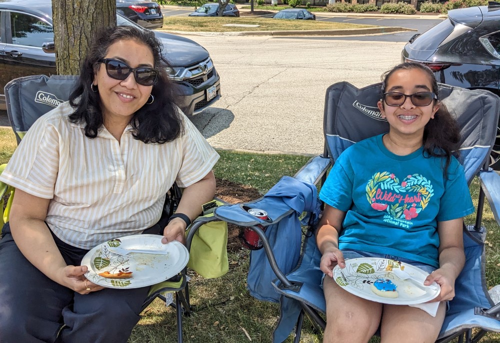 Woman and girl sit under a tree with plates of food