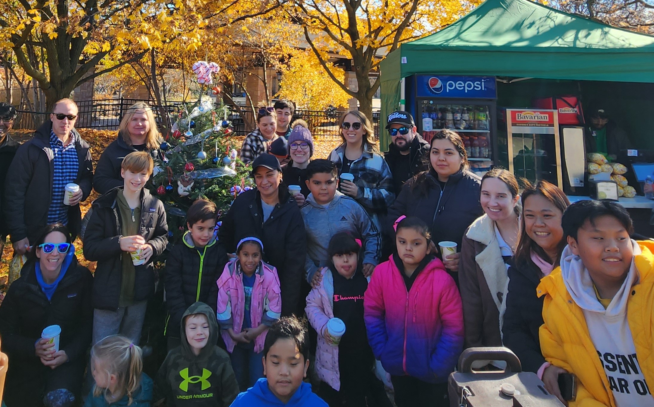 A group stands in front of a holiday tree on a sunny day