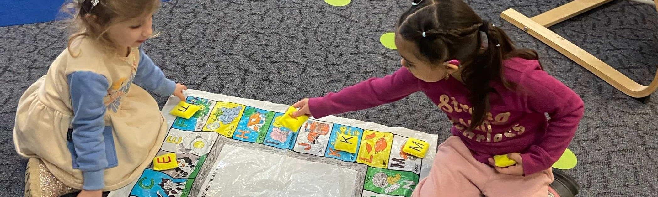 Two young girls play a word game on the floor