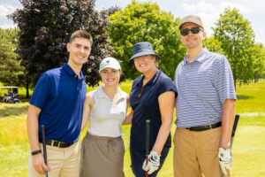 Four adults smile at the camera on a golf course