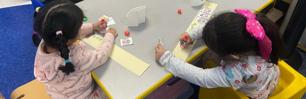 Two little girls making paper hats are shown from the back