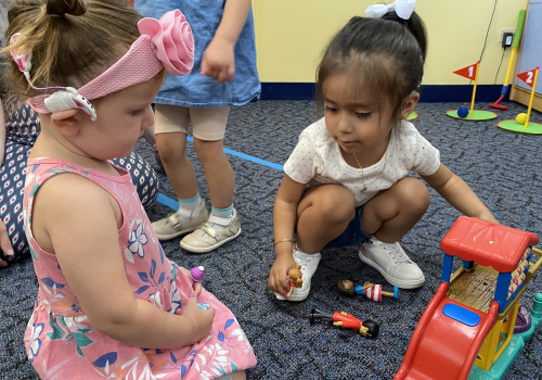 Two little girls play with toys on a classroom floor